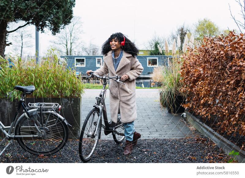 Cheerful black woman in headphones with bicycle using music listen bike chill city female african american woman street smile walk stroll positive rest autumn