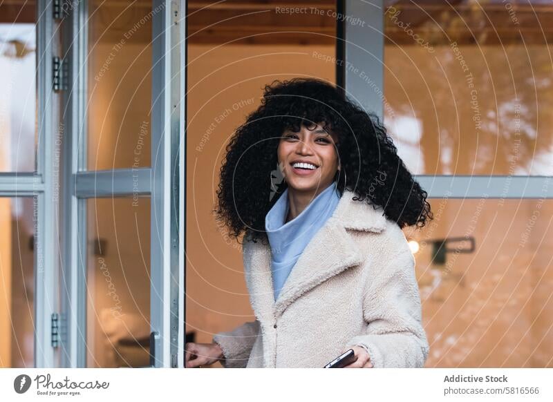 Happy black woman standing in doorway of house home walking out warm clothes coat outerwear urban female african american woman personality entrance young