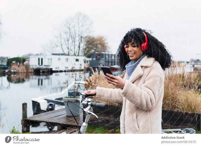 Delighted black woman with smartphone on bicycle headphones using music listen walk ride bike chill female african american woman city portrait street smile