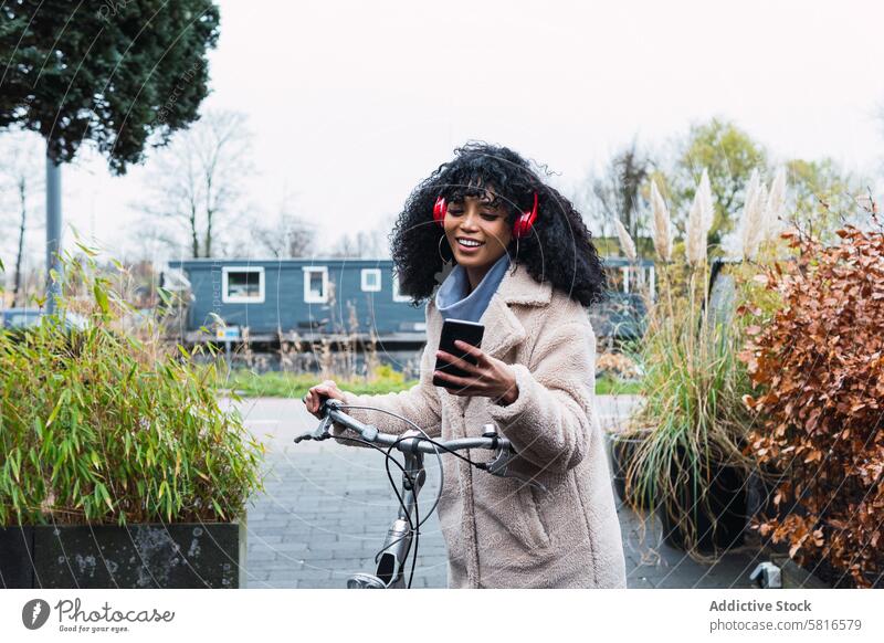 Black woman with smartphone on bicycle headphones using music listen ride bike chill female african american woman black woman relax city portrait street smile