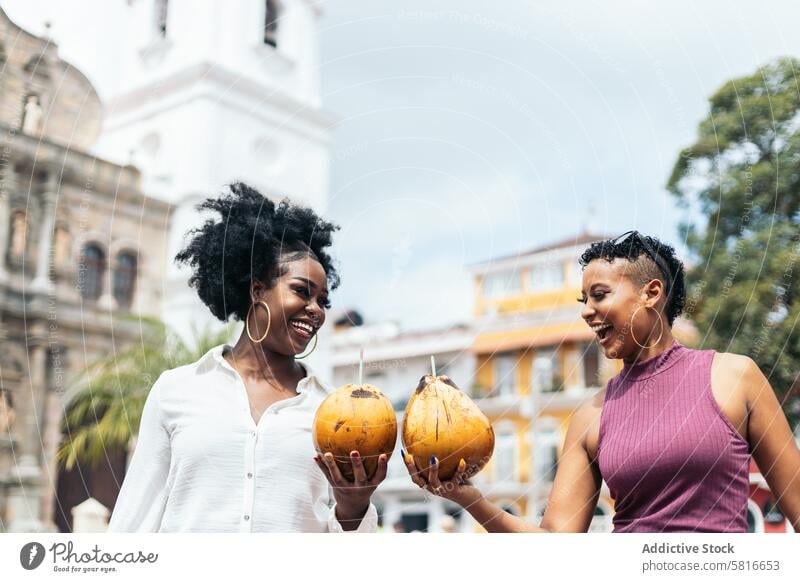 Latin American women having fun in the city drinking coconuts happy young summer female outdoors people leisure lifestyle joyful spring enjoyment hair curly