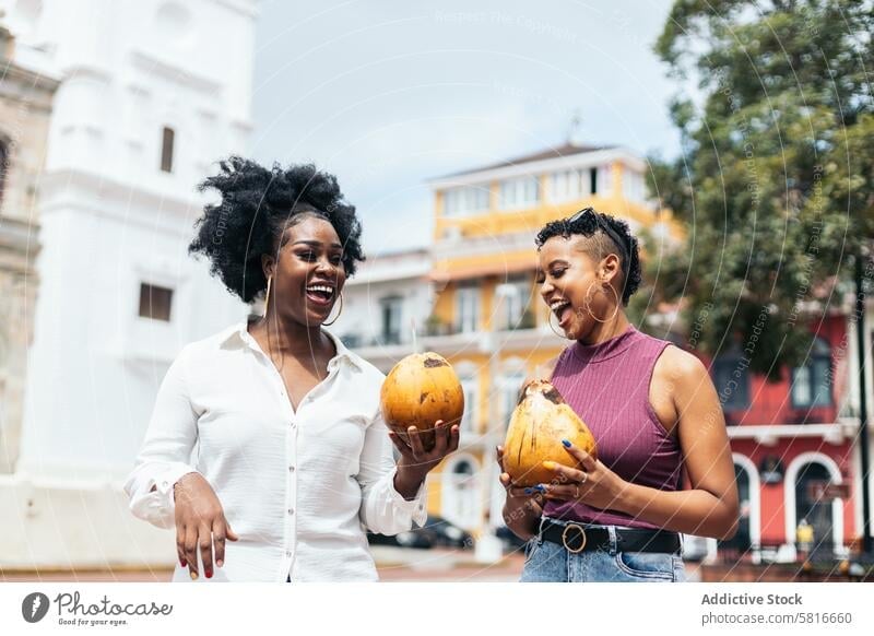 Latin American women having fun in the city drinking coconuts happy young summer female outdoors people leisure lifestyle joyful spring enjoyment hair curly