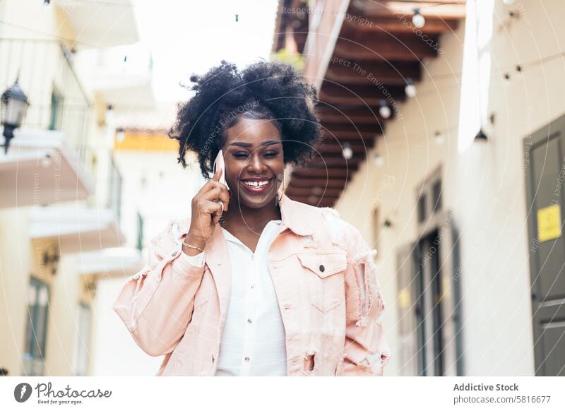 Stylish black woman walking on the city street talking on the phone young female outdoors urban fashion beautiful lifestyle casual people hair attractive curly