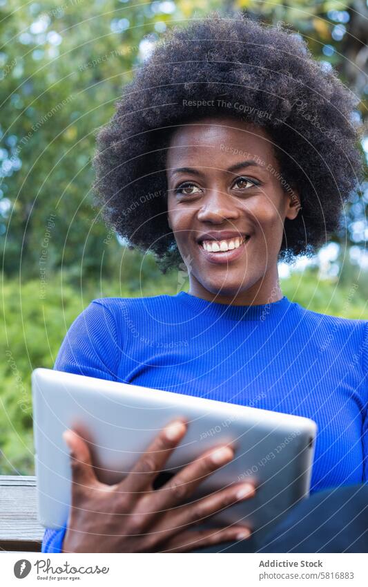 Smiling black woman browsing tablet in city startup freelance remote work park using smile female ethnic african american content gadget device connection bench