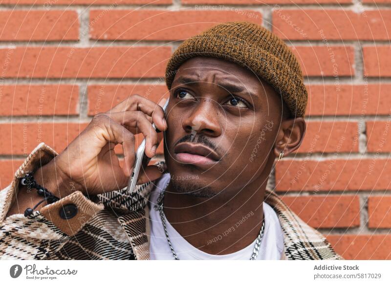 Ethnic guy speaking on smartphone near brick wall man street city urban lean casual male young black ethnic african american conversation modern connection