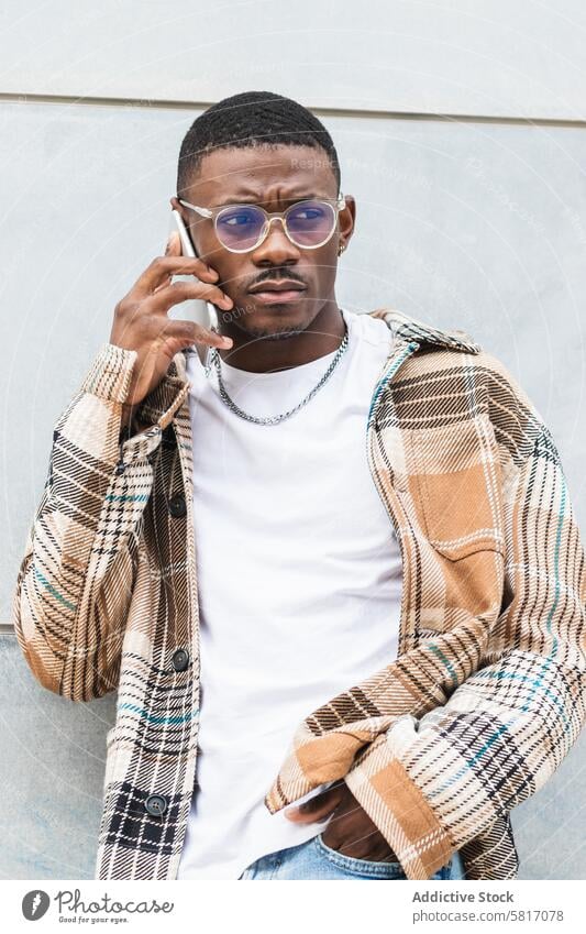 Stylish black male using smartphone on street man talk speak city wall style outfit young urban trendy ethnic african american gadget casual glasses