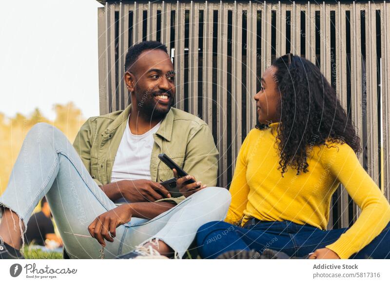 black couple sitting in a park using mobile young phone friends internet online man woman smartphone outdoors african leisure people lifestyle smiling beautiful