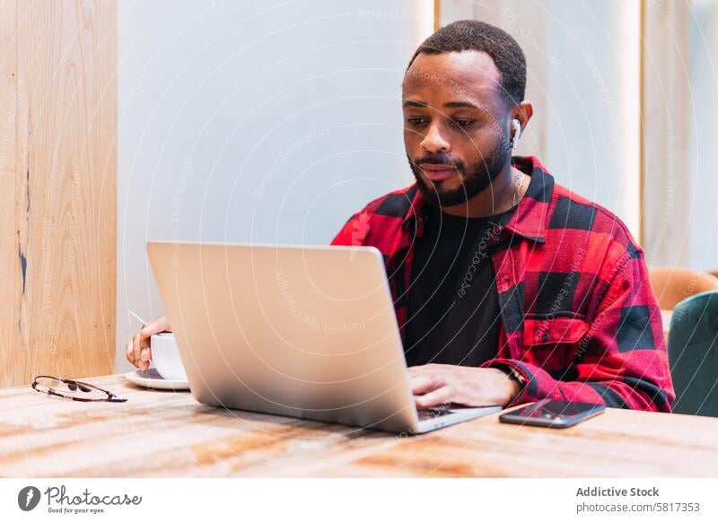 Black man working on laptop in cafe earphones using online internet browsing freelance male black african american netbook surfing coffee remote connection