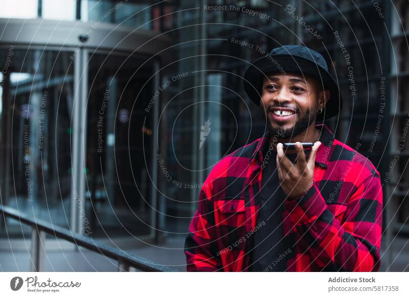 Cheerful black man talking on smartphone on street voice message using city communicate audio online internet urban male african american call beard smile