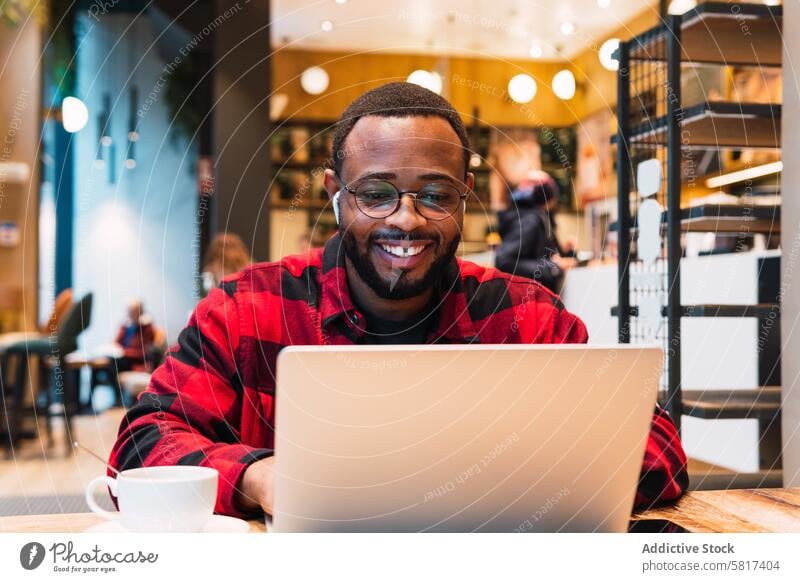 Smiling black man working on laptop in cafe earphones using online internet browsing freelance male african american netbook surfing coffee remote connection
