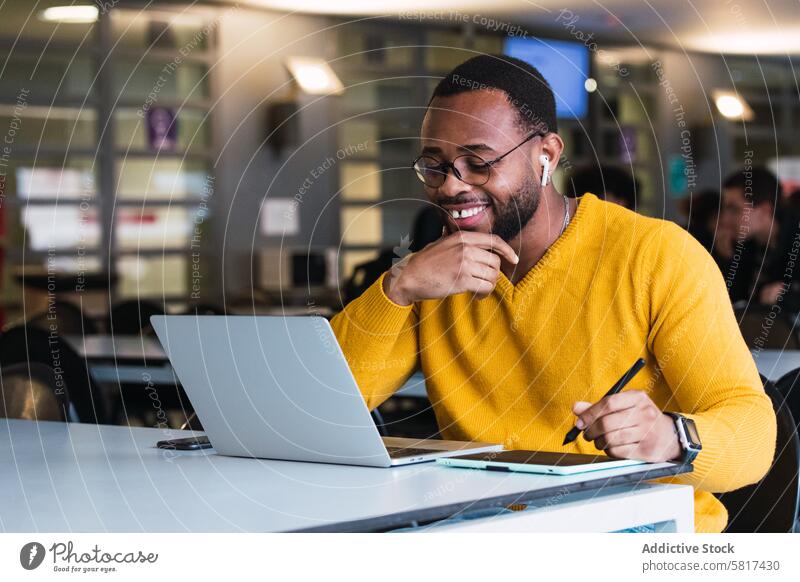 Smiling black man working on laptop with tablet graphic tablet designer earphones using online internet office take note male african american netbook