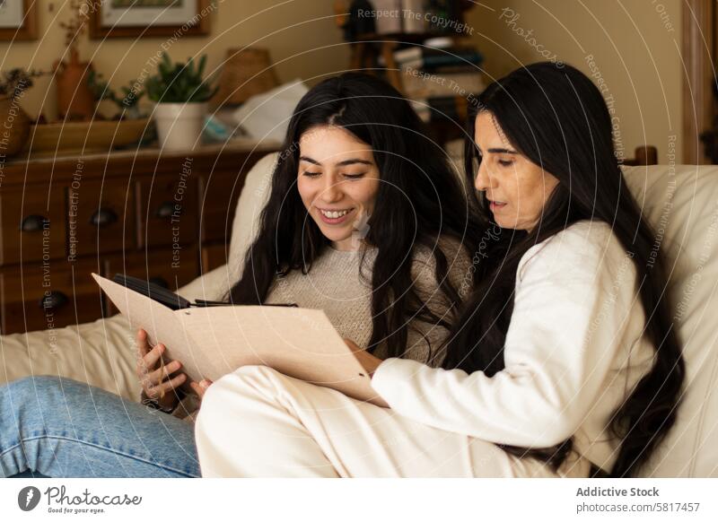 Mature mother and adult daughter watching a photo album home woman together young child happy female people parent house book sitting family looking kid holding