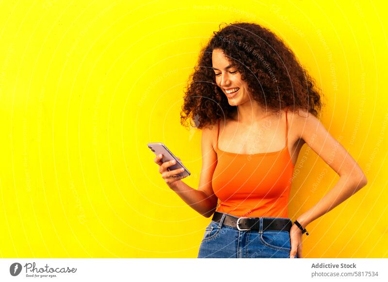 stylish afro woman using her mobile leaning on a yellow wall technology young person people phone smartphone african watching happy lifestyle device digital