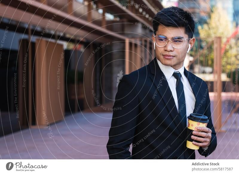 Handsome ethnic businessman with takeaway coffee in city handsome suit entrepreneur to go masculine street male asian wireless earbuds beverage drink paper cup