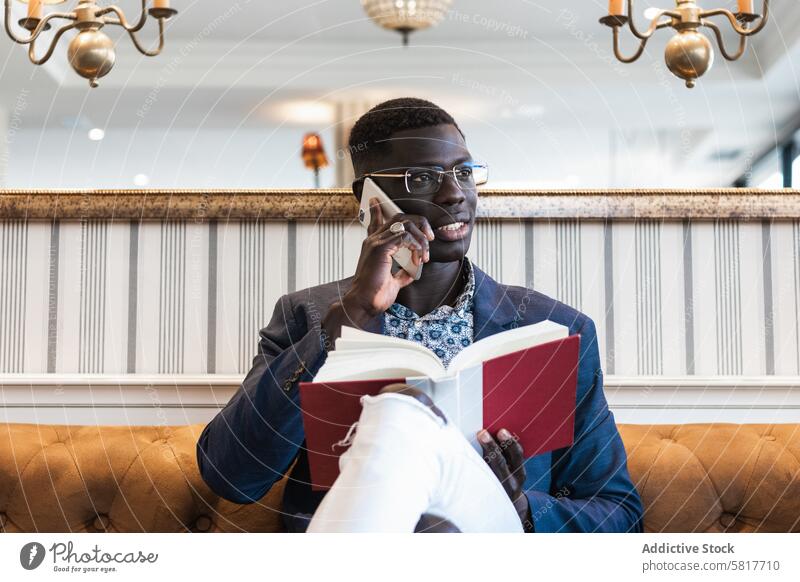 Stylish black businessman speaking on smartphone on sofa executive independent agenda smile legs crossed using gadget device cellphone reflection table couch