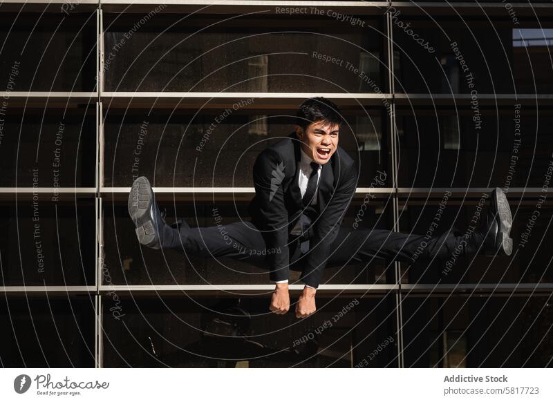 Businessman jumping in splits in city businessman shout rebel entrepreneur confident yell furious scream ambition male ethnic asian formal suit glass building