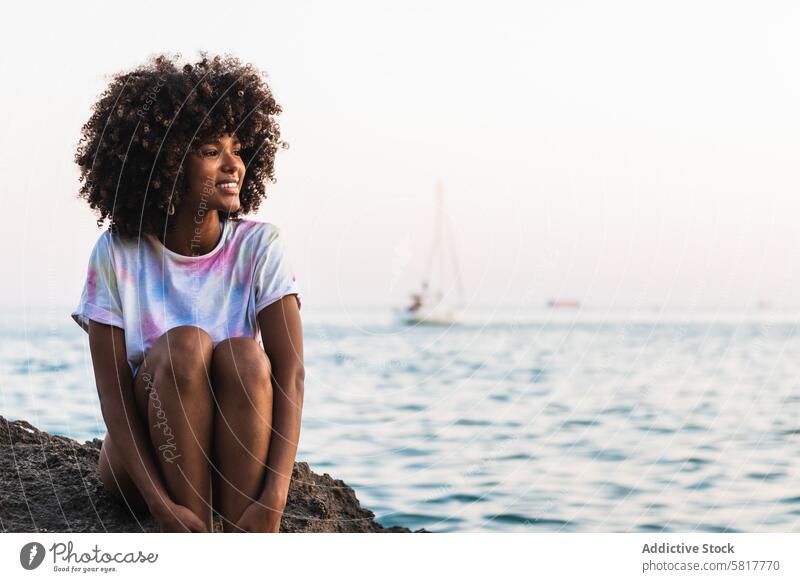 Delighted ethnic woman laughing at seaside beach summer seashore slim afro hairstyle having fun female black african american rock sit t shirt positive happy