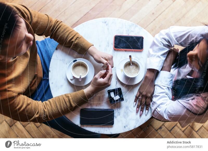 Overhead shot of two people on a date drinking coffee table overhead top view cup coffee shop cafe lifestyle concept smartphone mobile phone technology sugar