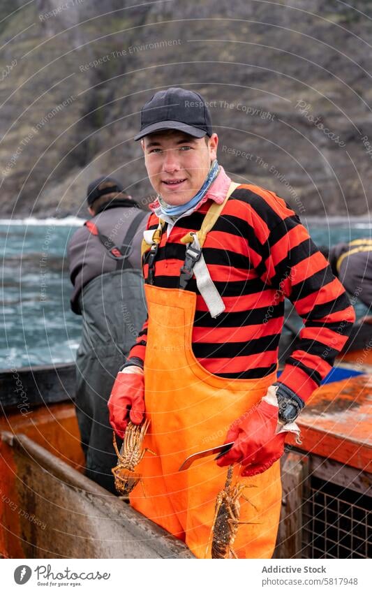 Portrait of a young fisherman in apron working holding lobsters vertical portrait caucasian smiling looking at camera stand gloves maritime seafaring aquatic