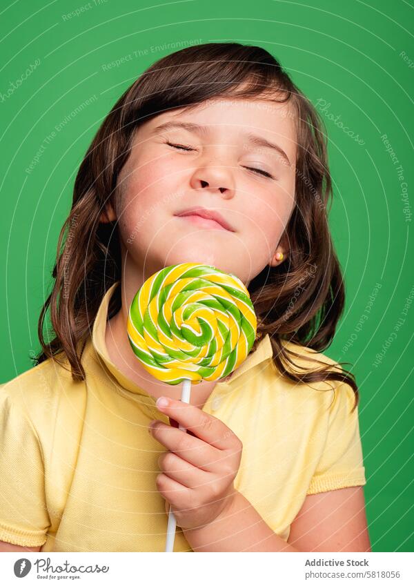 Content girl with eyes closed holding a lollipop content studio shot child pleasure scent young colorful green background innocence enjoyment smelling