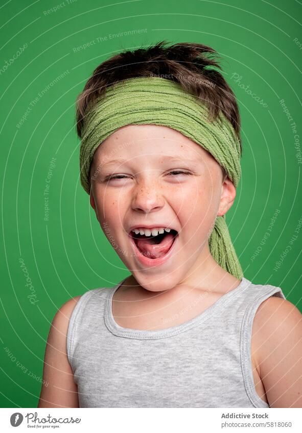 Cheerful boy winking and shouting in studio child studio shot looking at camera cheerful happy excitement joy energy green background freckles headband tank top