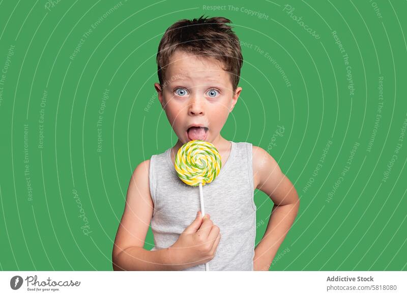 Surprised young boy with lollipop on green background child surprised studio shot looking at camera emotion excitement amazement candy sweet snack dessert treat