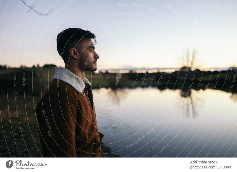 Young man watching the sunset at a lake in the countryside nature water copy space natural light outdoors landscape scene serenity view lifestyle field winter