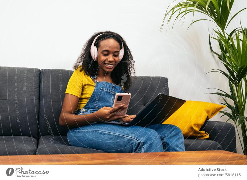 Young black woman working with laptop and enjoying music at home Digital lifestyle Technology Black woman Tablet Cozy home Minimalist decor Browsing Streaming