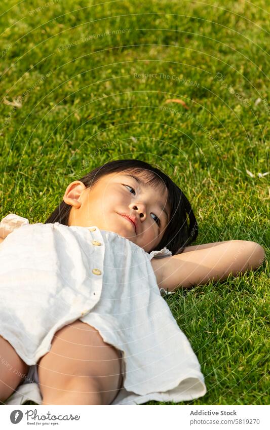 Asian child relaxing on grass during European vacation asian girl europe leisure holiday family joy dreamy nature travel outdoors serenity calm peaceful rest