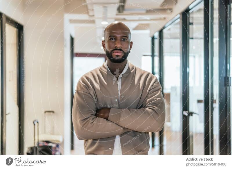 Confident entrepreneur in modern coworking space male office professional business workspace self-assured arms crossed business attire contemporary ethnic