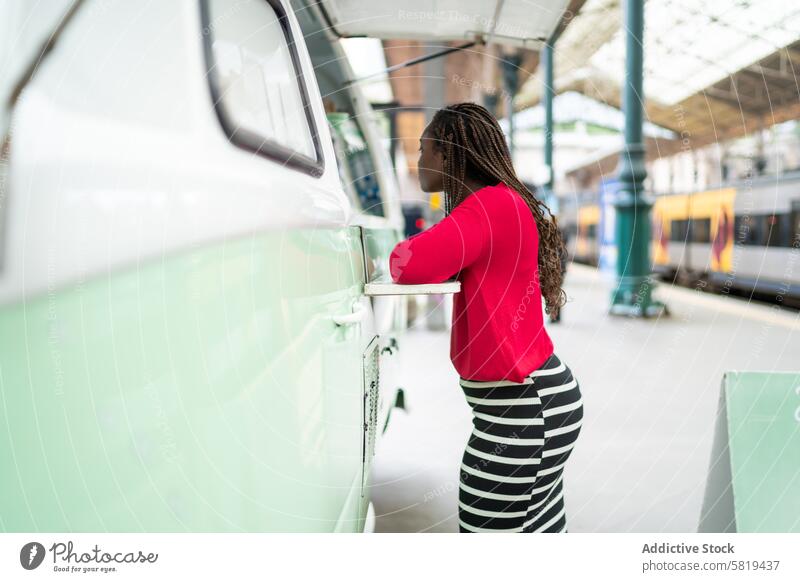 Black Woman boarding a train at a busy station woman commute urban travel transport city red top striped pants platform rail passenger public girl journey