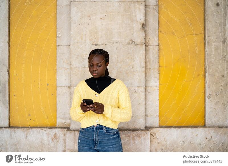 Young woman in yellow sweater texting on smartphone concrete wall jeans young vibrant focus outdoor technology communication casual attire fashion style urban