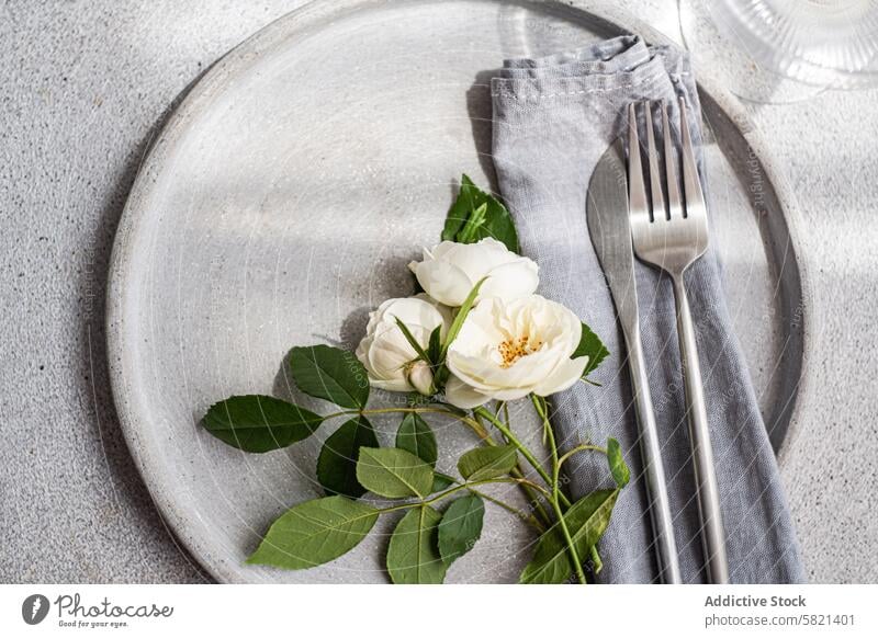 Elegant neutral table setting with fresh white roses ceramic plate silver cutlery linen napkin flower arrangement wedding elegant dining decor fork knife