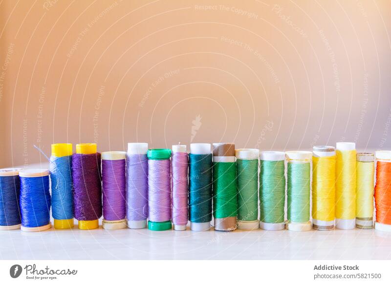 Vibrant Thread Spools Lined Up on Neutral Background thread spool sewing color rainbow arrangement textile material fashion design workshop craft hobby