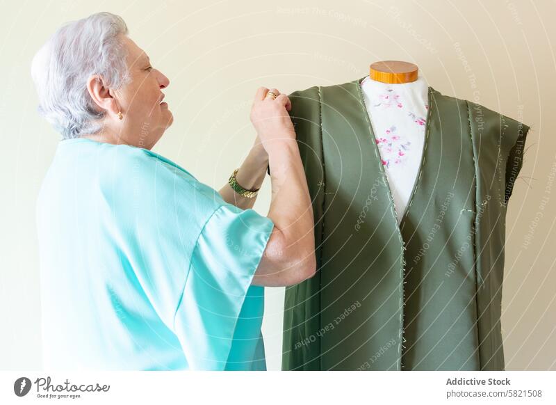 Elderly seamstress working on a garment on a mannequin elderly woman tailoring dress workshop sewing fabric craftsmanship designer fashion textile clothing