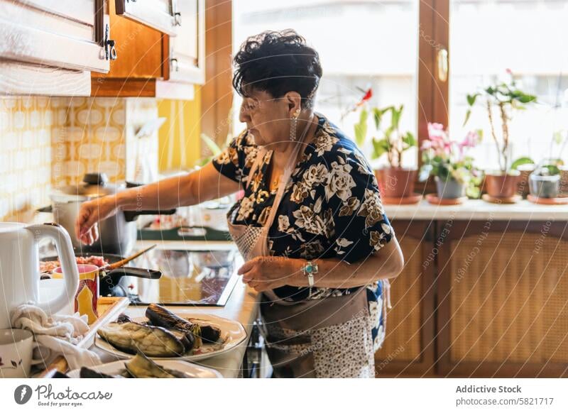 Elderly Lady Preparing a Meal in a Homely Kitchen senior woman cooking kitchen home vegetables utensils elderly meal preparation homely cookware stove apron