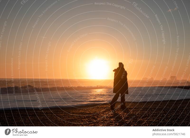 Silhouette of a person walking on a beach at sunrise in Iceland iceland silhouette sea horizon wave shore tranquil serene morning light bright glow landscape