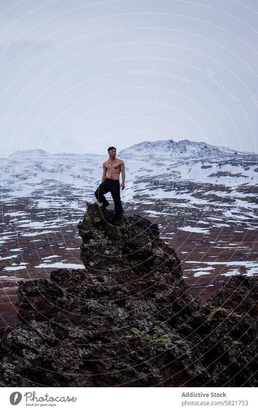 Man standing shirtless atop a rocky outcrop in snowy Iceland man iceland mountain outdoor adventure rugged landscape wilderness cold winter travel volcanic