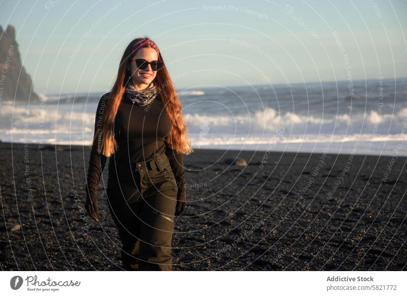 Young woman exploring the black sand beach in Iceland iceland volcanic sunglasses hiking casual style outdoor adventure travel tourism sunny waves crashing