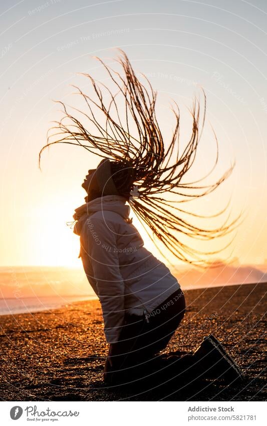 Woman with flowing hair at sunset on an Icelandic beach woman silhouette iceland wind dramatic serene glowing horizon ocean winter dusk tranquil peace outdoor