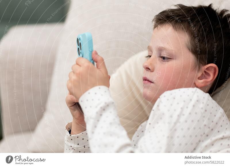 Boy at home focused on smartphone screen child boy technology lounge sofa relax leisure indoor device mobile engagement sitting casual comfort living room