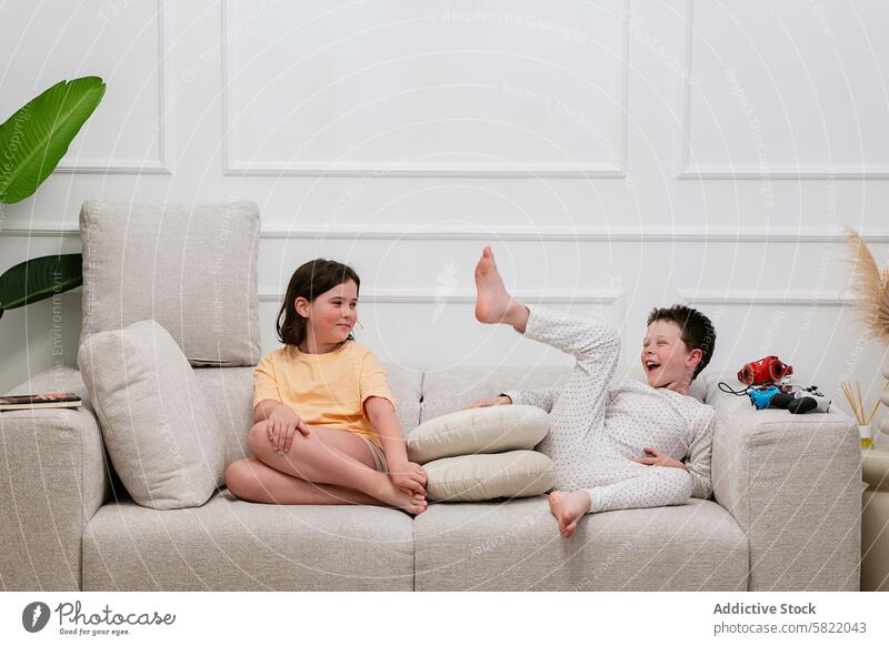 Sibling fun on couch, girl watches boy's antics sibling home laughing watching amusement indoor living room sofa kid child domestic life family playful joy