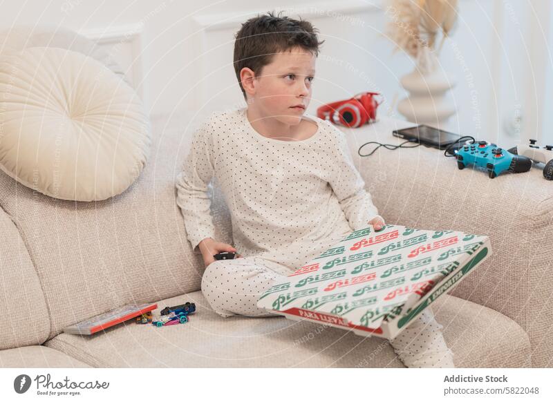 Casual boy with pizza at home looking away sofa box casual lounge look away youth child domestic indoor comfort cozy food snack living room childhood leisure