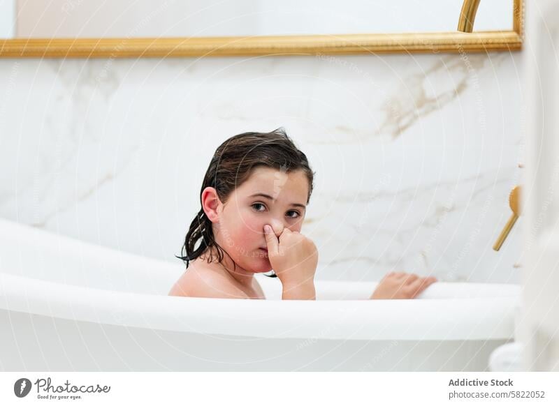 Young girl playing in bath at home, looking at camera child bathtub bathroom wet hair indoor hygiene clean water playful childhood marble mirror fun candid