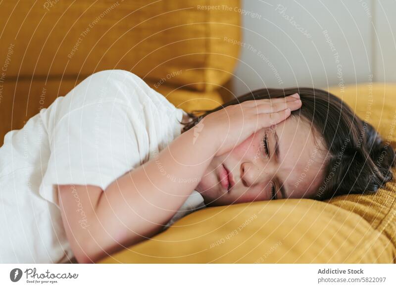 Young girl experiencing headache while resting on couch yellow child unwell symptom hypoglycemia illness health discomfort pain indoor home care medical hand