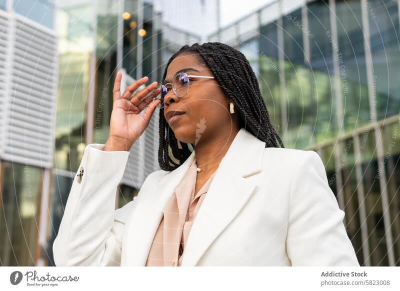 Confident professional woman in urban setting confident chic blazer glasses business fashion modern city building reflective african american poise elegance