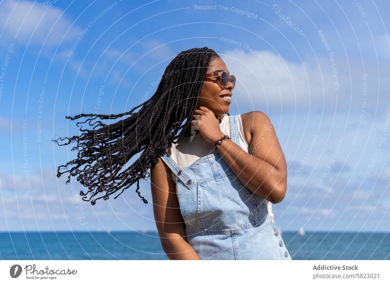 Joyful Summer Day by the Sea in Barcelona woman summer sea barcelona coastline sunny blue sky denim overalls glasses smile happy hairstyle braids african youth