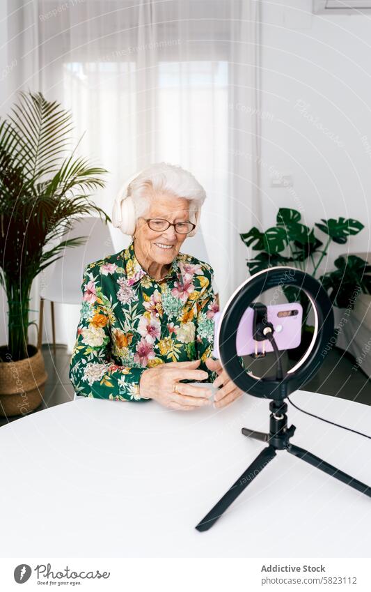 Elderly woman recording a podcast with modern equipment elderly headphone smartphone ring light smile joyful influencer technology indoor happy senior media