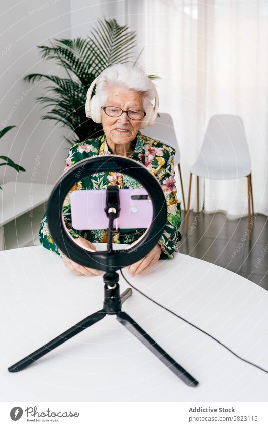 Elderly woman records podcast with modern equipment elderly recording headphones smartphone ring light technology influencer media content creation digital