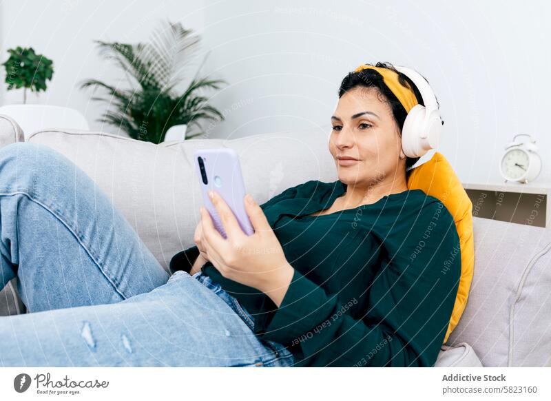 Woman enjoying music and browsing on smartphone at home woman headphones sofa leisure relaxed cozy technology connectivity mobile device app online streaming